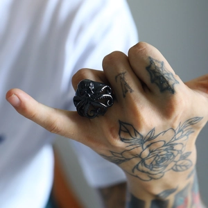 Detailaufnahme eines schwarzen Oktopus-Rings mit Saugnäpfen an einer tätowierten Hand