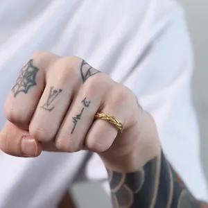 Minimalist woven twist stainless steel ring in gold finish on male hand with tattoo