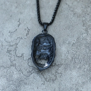 Close-up of matte black punk skull pendant on gray stone background with box chain