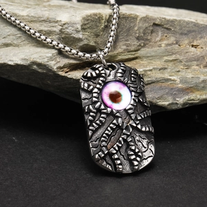Detalle del colgante punk con ojo de demonio y texturas mecánicas sobre fondo oscuro
