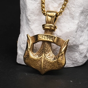 Détail d'un pendentif ancre dorée vintage avec gravure CHINA et chaîne maille sur pierre