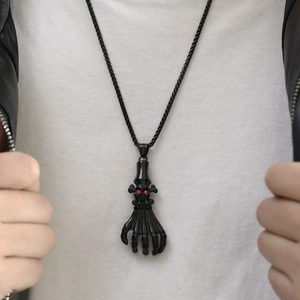 Detail of punk skeleton hand pendant with red eye skull on black beaded chain necklace