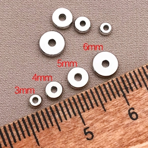 Vista macro de cuentas espaciadoras plateadas de 3mm a 6mm sobre tela gris rugosa