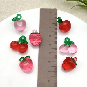 Detailed macro view of resin strawberry and cherry charms next to a metric ruler