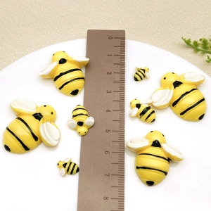 Mini abeilles en résine de tailles variées sur fond blanc avec règle pour les dimensions