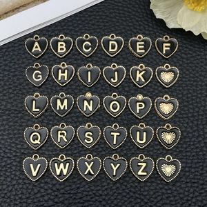 Macro-opname van zwarte emaille hartbedeltjes met gouden letters A-Z voor DIY-sieraden