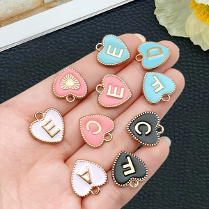 Hand met hartvormige emaille letterhangers met gouden kralenrand voor DIY-sieraden