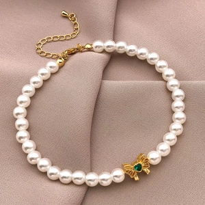 Elegant pearl necklace featuring an 18K gold-plated bow pendant with a green heart gemstone