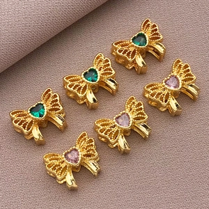 Macro detail of 18K gold plated bow beads with heart-shaped emerald and purple zircons