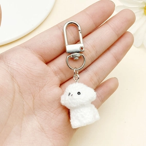 Detailed view of white fluffy dog pendant with silver metal clasp held in hand