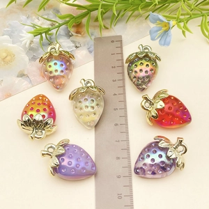 Macro shot of colorful acrylic strawberry charms with golden leaves beside a ruler