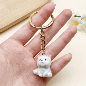 Detailed view of a mini white flocked dog keychain with golden hardware in hand