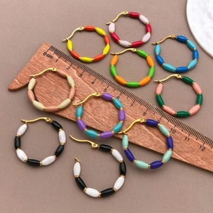 Macro shot of colorful enamel bamboo-style U-shaped hoop earrings next to a wooden ruler