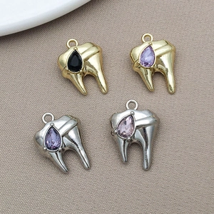 Dettaglio di ciondoli a forma di dente in lega con strass, placcati in oro e argento