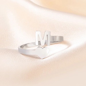 Makroaufnahme von poliertem Edelstahlring mit M-Buchstabe und Herz auf Seidenhintergrund