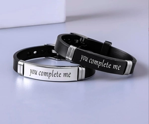 Detail of couple bracelets featuring you complete me engraving on steel plates