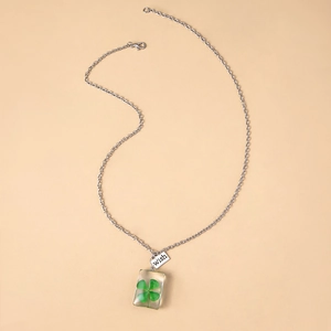 Detail of silver chain necklace with real four-leaf clover resin pendant and 'wish' charm
