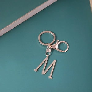 Porte-clés lettre M en or rose poli avec fermoir mousqueton sur fond sombre texturé