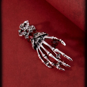 Gothic silver skeleton hand brooch with red rhinestones on a dark textured background