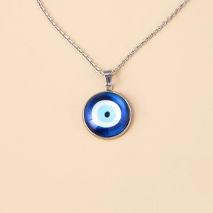 Macro shot of blue glass evil eye pendant with silver chain on beige background
