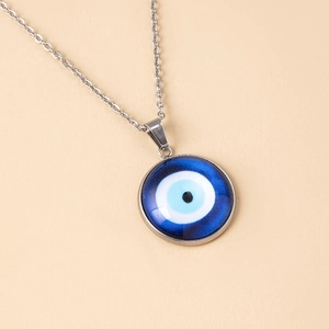 Close-up of blue glass evil eye pendant with silver chain on light pink background