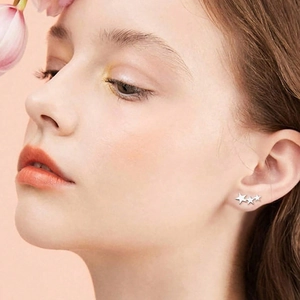 Eleganti orecchini a lobo in argento con tre stelle indossati su sfondo rosa tenue