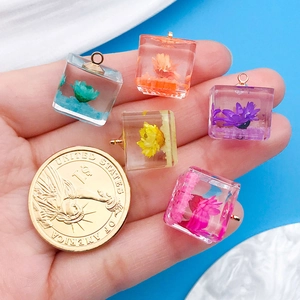Detailed view of colorful resin cubes with dried flowers held next to a dollar coin