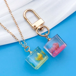 Macro detail of cube resin pendants with real dried flowers on gold chains and keyrings