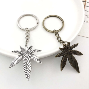 Close-up of silver and bronze cannabis leaf pendants with metal keyrings in a ceramic tray