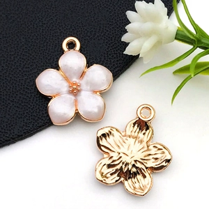 Détail de breloques fleurs en or rose avec émail blanc et dos en métal texturé de qualité