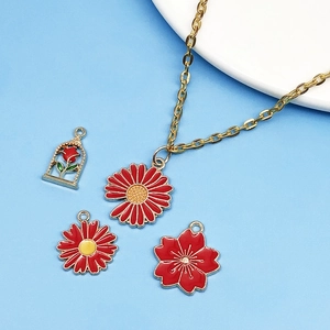 Détail de breloques émaillées rouges rose et marguerite sur collier doré sur fond bleu