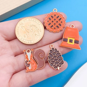 Detail of autumn enamel pendants with pine cone and pumpkin next to a coin for size