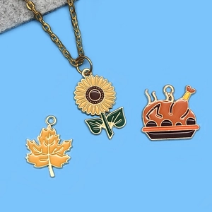 Detalle de colgantes de esmalte arce, girasol y pavo con collar dorado para manualidad