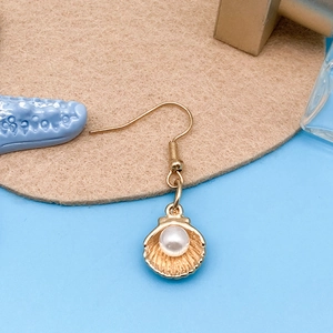 Close-up of golden alloy scallop shell earrings with white pearl detail on felt background