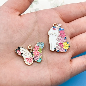 Macro detail of handmade enamel butterfly and cat charms with floral accents on a palm