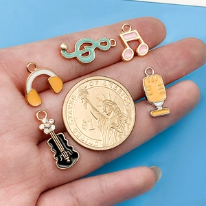 Enameled music charms including guitar and piano notes next to a dollar coin for scale