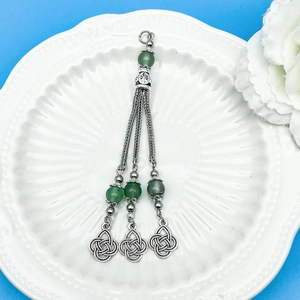 Green beaded tassel pendant with Celtic knot charms on a white decorative ceramic plate