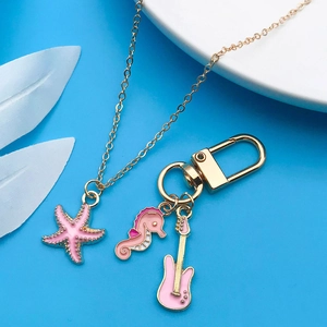 Pink enamel unicorn and guitar alloy pendants with gold chain on blue surface