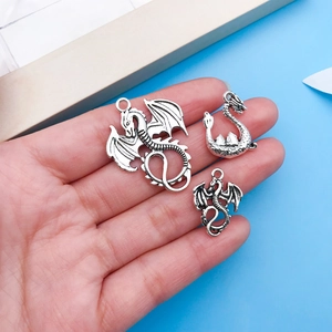 Macro detail of three vintage silver dragon pendants held in hand to show small size