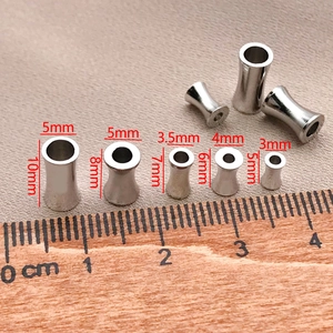 Silberne Zylinder-Zwischenperlen in Sanduhrform auf Holzlineal zur genauen Größenbestimmung