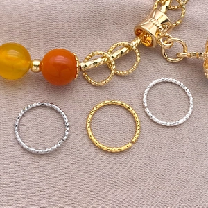 18K vergoldete Spiraldrehringe mit orangen Perlen auf lila Seidenhintergrund