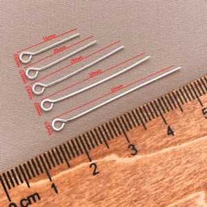 Detailed comparison of five sizes of 18K gold-plated eye pins with a wooden ruler