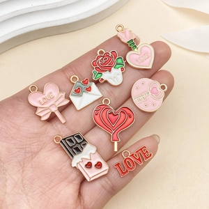 Primer plano de varios dijes esmaltados de San Valentín rosas y rojos en la mano