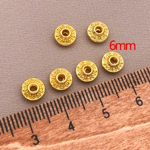 Detail of 6mm gold-plated saucer beads with spiral engraving on gray fabric background