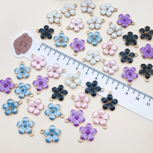 Detail of colorful enamel flower charms with gold alloy edges and a ruler for size scale