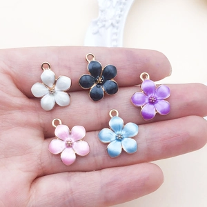 Detailed close-up of five colorful enamel cherry blossom charms held in a hand for DIY crafts