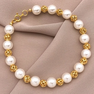 Gros plan détaillé des perles en maille dorée 18K et perles blanches sur tissu doux