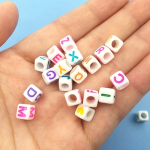Cuentas de letras acrílicas coloridas en cubos blancos para joyería DIY en una mano palma