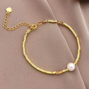 Detail of 18K gold-plated square beads bracelet with a white pearl and heart pendant