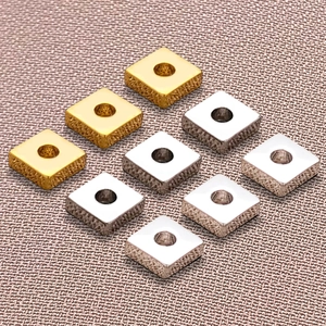Macro shot of square gold and silver metal spacer beads on a textured purple fabric background